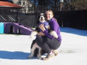 Staff member outside in the snow hugging a dog